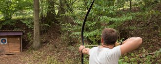 Im Wald: ein Mann zielt mit Pfeil und Bogen auf eine Zielscheibe 