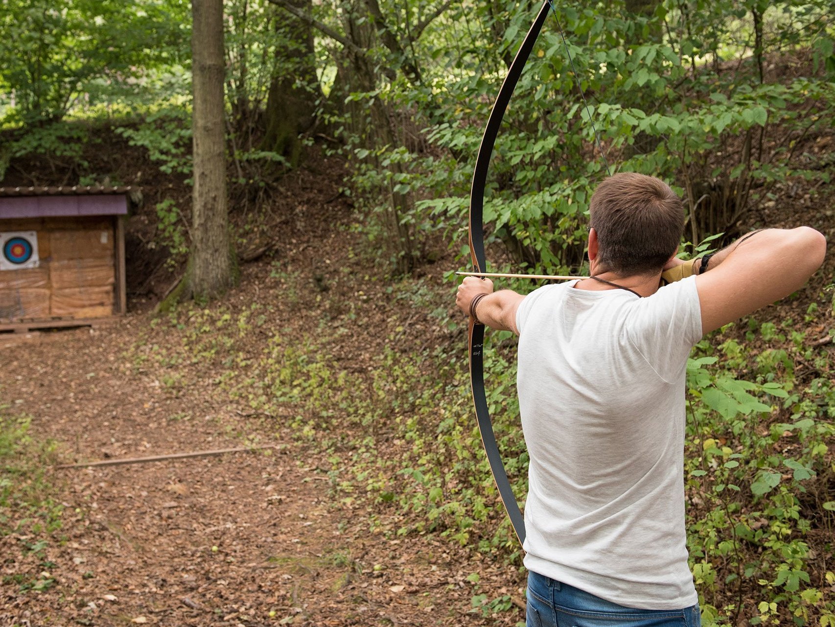 Im Wald: ein Mann zielt mit Pfeil und Bogen auf eine Zielscheibe 