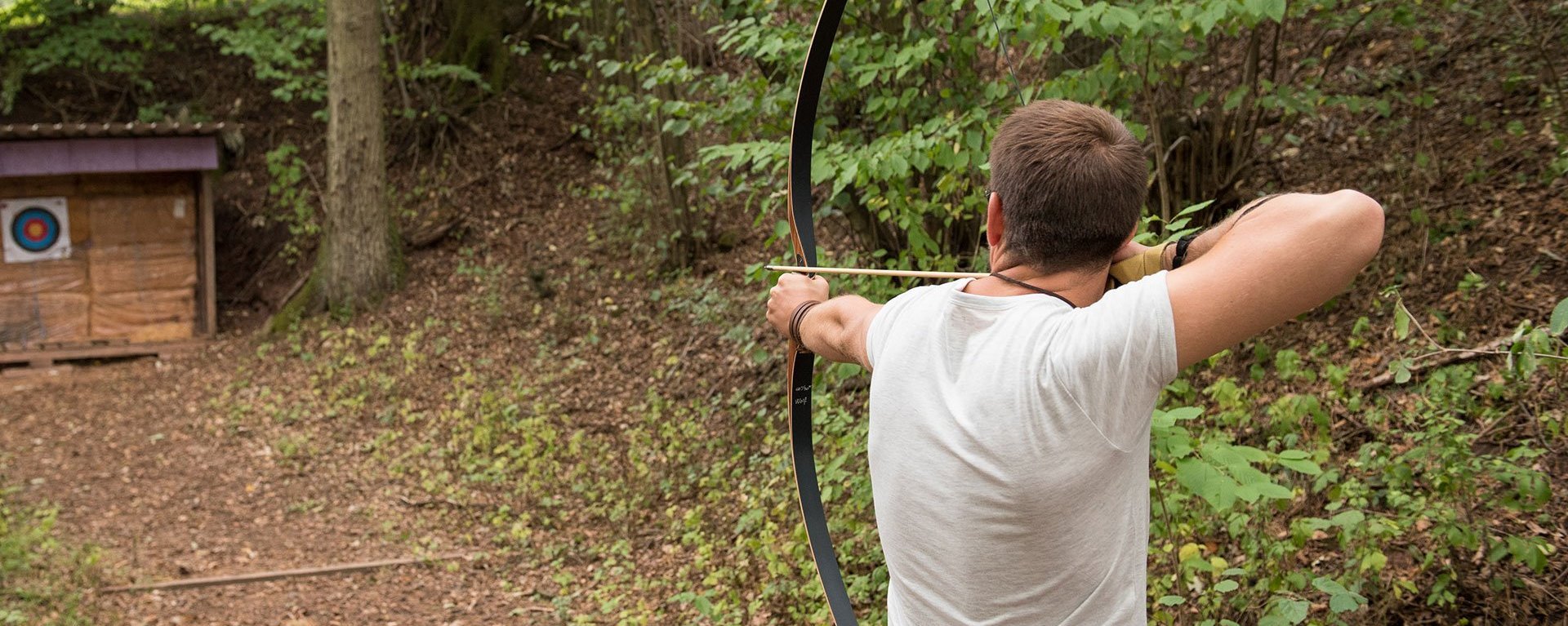 Im Wald: ein Mann zielt mit Pfeil und Bogen auf eine Zielscheibe 