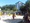 Eine Gruppe von Männern spielt Beachvolleyball auf einem Sandplatz an einem sonnigen Tag. Ein gelbes Netz teilt das Spielfeld. Im Hintergrund sind Bäume und ein weißes Gebäude zu sehen, während Zuschauer das Spiel beobachten.