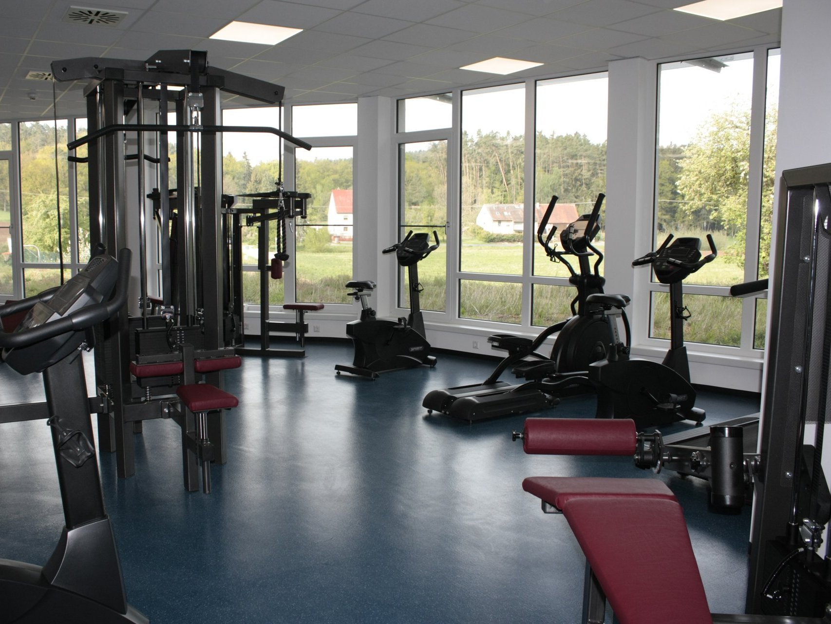 Sport: im Fitnessraum mit großen Fenstern stehen verschiedene Sportgeräte (Laufbänder, Crosstrainer, Spinner,...)