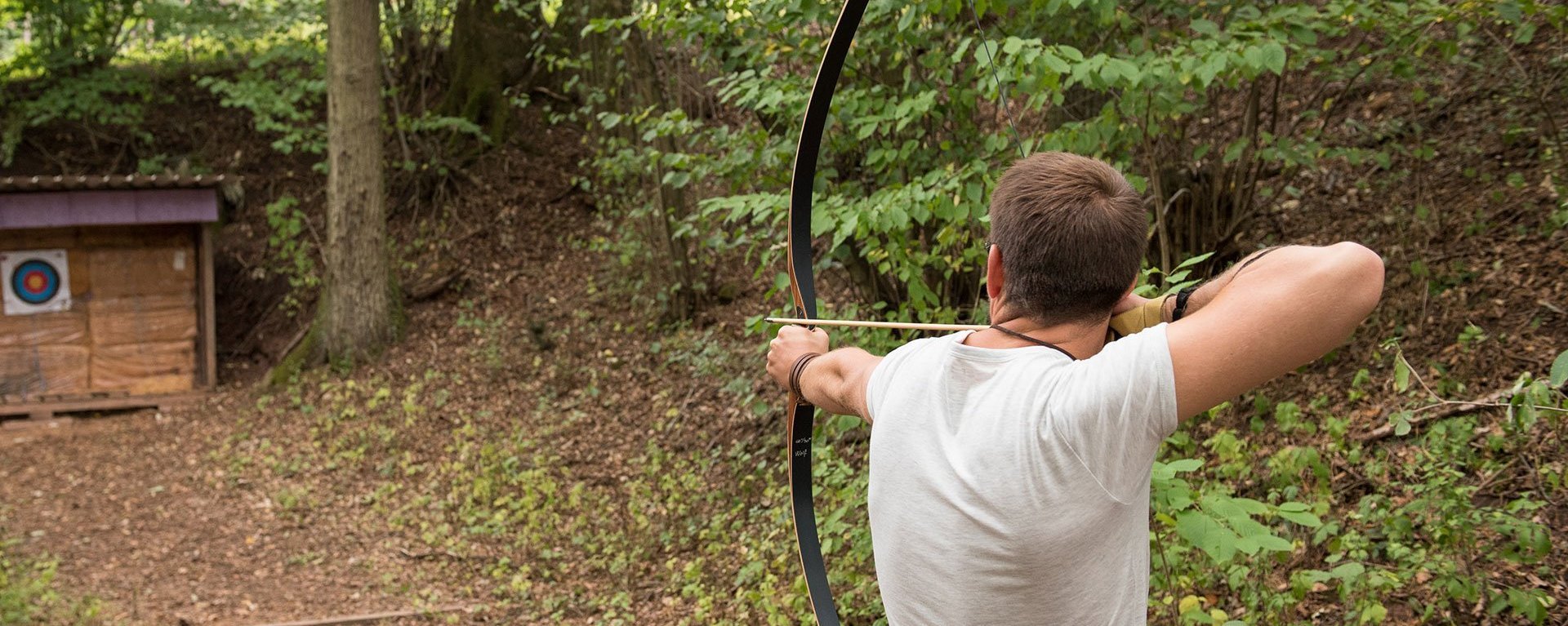 Im Wald: ein Mann zielt mit Pfeil und Bogen auf eine Zielscheibe 